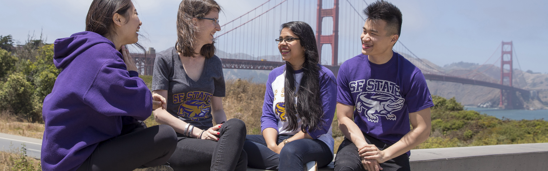 Four students sitting close together in front of the Golden Gate Bridge.